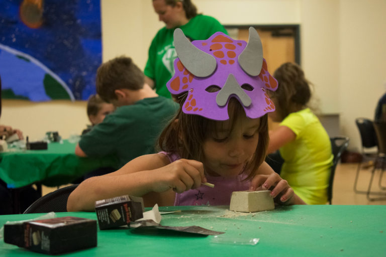 A small girl in a dinosaur mask "excavating" fossils