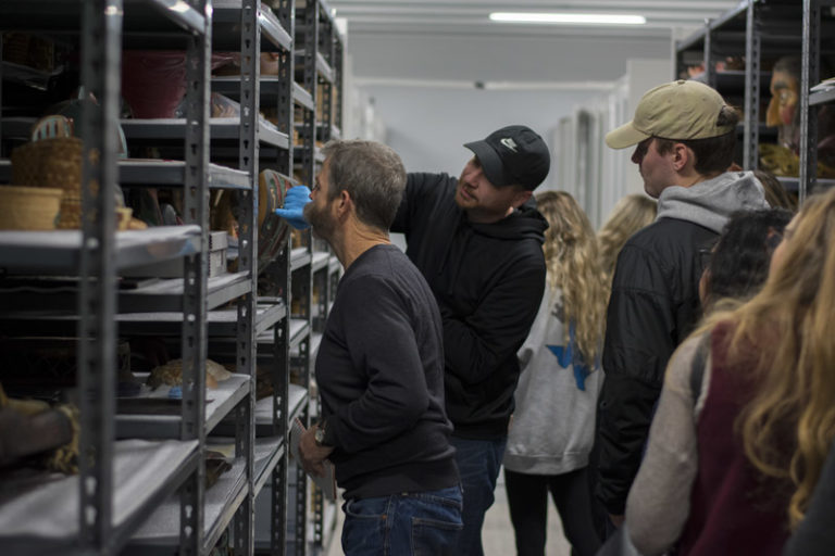 A curator shows collections to a group of students and their teacher